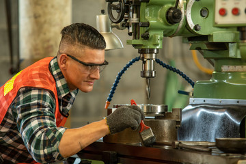 Mechanical engineer wearing safety harness use milling machine in workshop.