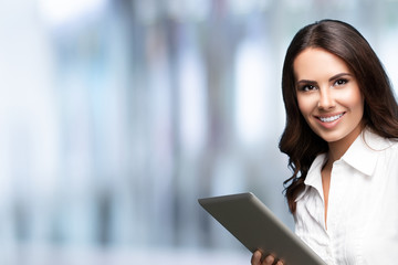 Sticker - Happy smiling beautiful young brunette businesswoman using no-name tablet pc, against blurred office background, with copy space for some slogan or text. Success in business concept.