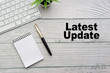 © instagram.com/_alfil - LATEST UPDATE text with notepad, keyboard, decorative vase and fountain pen on wooden background. Business and copy space concept