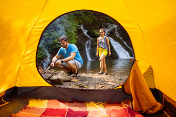 Wall Mural - couple resting at lake beach with waterfall view from yellow tent