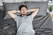 © pressmaster - Young bearded man lying with hands behind head while sleeping alone in bed