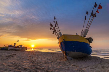 Wall Mural - Colorful fishing boat on a sandy sea beach during a beautiful sunset