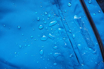 Closeup of water drops on bright blue fabric and black zipper with waterproof design to protect fabric of the cloth from humidity and to offer easy cleaning to users Fabric texture with design concept