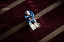 Young Arabic Muslim Man Reading Koran And Praying. Religious Muslim Man Reading Holy Koran Inside The Mosque.