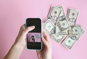 Wall Mural - 1, 5, 20 dollars are lying in a mess on a pink background, they are removed from the top of the smartphone, top view