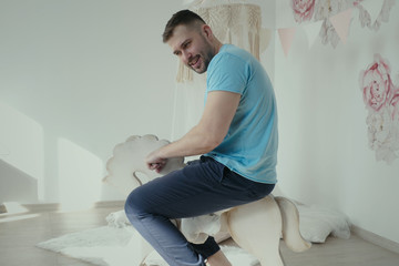 Adult autistic man riding a toy horse in child room, smiling man wearing casual clothes riding on toy wooden horse