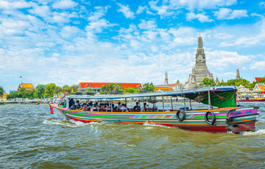 View over river Chao Phraya from boat back to temple Wat Arun, eldest temple in Bangkok. In foreground is speed longboat passing. Behind are tour boats and ferries. 