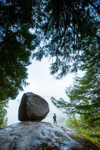 Woman Hiker Standing Next To Big Boulder With Trees Framing Her In The Fog Of Squamish.