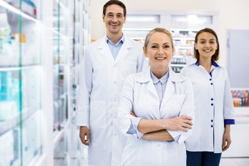 Wall Mural - Happy three young pharmacists welcoming customers smiling