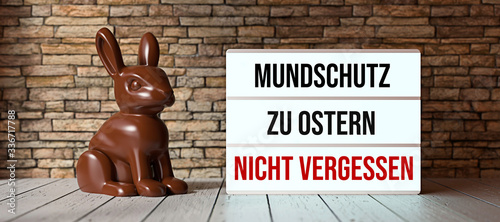 chocolate bunny and lightbox with German message for DON\'T FORGET FACE MASK AT EASTER in front of a brick wall