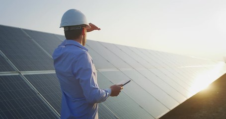 Wall Mural - an young engineer is checking with tablet an operation of sun and cleanliness on field of photovolta