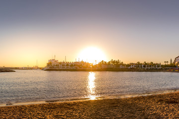 Wall Mural - Sunset over the lagoon of orange-red clouds on the horizon and reflections of lights reflecting on sea level with urban area Grand Canary Island Valle