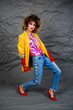 © Михаил Гута - Girl in a yellow jacket and blue jeans with an afro hairstyle. Fashion of the eighties, disco era. Studio photo on gray background.