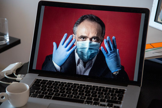 Laptop con dentro un immagine di uomo in giacca con guanti in lattine e mascherina protettrice , contestualizzato in una postazione di lavoro con altri elementi quali monitor 