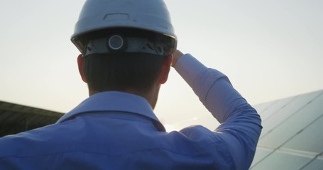 Wall Mural - an young engineer is watching a sunset satisfied with his job on a background of solar panel field. 