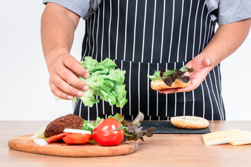 The butler is cooking a hamburger Which contains fres vegetables, meat and sheese, Is a food that is easy to make And nutritious, On white background to people and food concept.