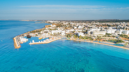 Wall Mural - Aerial bird's eye view of Pantachou - Limanaki beach (Kaliva), Ayia Napa, Famagusta, Cyprus. Bay with golden sand, small fishing port, sunbeds, parasols, sea bar restaurants in Agia Napa, from above.