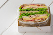 Club sandwich with ham, cheese, lettuce, and tomato served  in white paper in white box. Tasty homemade lunch, breakfast or take away food. Copy space.