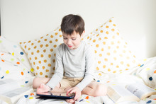 Game. Boy Plays With Smartphone. School Boy On Bed At Home With Digital Pad Tablet In Hand, Doing Homework. Distance Learning Online Education. Quarantine. Game. Boy Plays With Smartphone