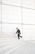 © PeskyMonkey - Distant businessman running outdoors up a long white staircase