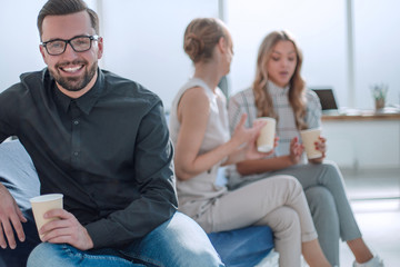 Poster - young businessman with a Cup of coffee sitting in a modern office.