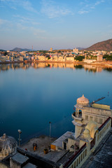 Fototapete - View of famous indian hinduism pilgrimage town sacred holy hindu religious city Pushkar amongst hills with Brahma mandir temple, lake and traditional Pushkar ghats at dusk sunset. Rajasthan, India