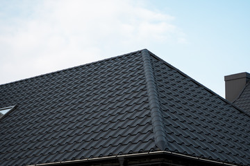 Wall Mural - Black metal tile roof. Roof metal sheets. Modern types of roofing materials. Roof of the house, metal roof tile against the blue sky. Building.