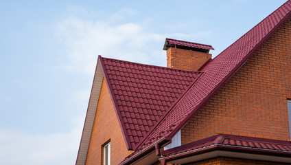 Wall Mural - Red metal tile roof. Roof metal sheets. Modern types of roofing materials. Roof of the house, metal roof tile against the blue sky. Building.