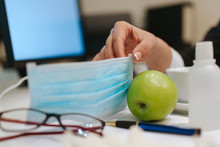 Glasses, Face Mask, Gloves, Hand Sanitizer And Apple On The Office Desk. COVID - 19 Virus Protection