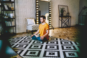 Fototapete - Young man doing easy seat yoga pose in living room