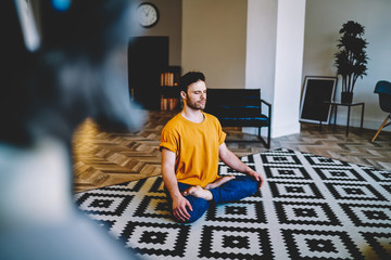 Fototapete - Young man calmly sitting on carpet and doing basic yoga exercises