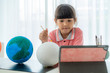 © ake1150 - Asian elementary schoolgirl painting the moon in science class learning about the solar system via video conference with teacher and other classmates at home, Homeschooling and distance learning..