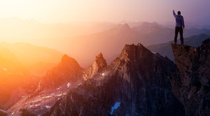 Wall Mural - Adventurous Man Hiker With Hands Up on top of a Steep Rocky Cliff. Sunset or Sunrise. Composite. Landscape Taken from British Columbia, Canada. Concept: Adventure, Explore, Hike, Lifestyle