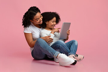 Black Mother And Daughter Using Digital Tablet, Sitting On Floor In Studio