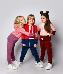 Wall Mural - Three frolic kids bonde and brunette girls and blond boy in stylish sportswear are posing together