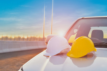 Wall Mural - White and yellow hard safety helmet hat in construction site on front of car for safety first concept of workman as engineer or worker on concrete floor on sunset background.