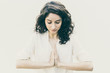 Concentrated woman meditating with hands in Namaste gesture. Wavy haired young woman in casual shirt standing isolated over white background. Yoga practice concept