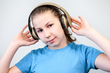 Cute child enjoying dance music, girl listening to music in headphones on grey background. Looking at camera