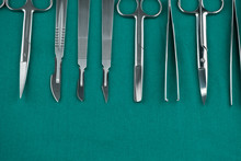 Basic Surgical Instrument Scalpel Forceps Tweezers Scissors On Surgical Green Drape Fabric In Operation Room