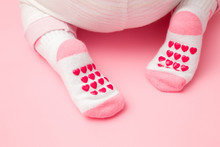 Baby Crawling On Light Pastel Pink Floor. Feet In Anti Slip Socks With Heart Shapes. Pastel Color. Closeup. Back View.