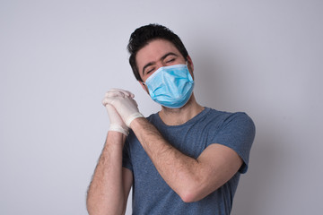 Wall Mural - Dreamy young male with pleasant expression, closes eyes, keeps hands crossed near face, thinks about something pleasant, poses against gray background.