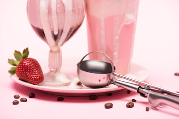 Wall Mural - Disposable cup and glass of milkshakes, strawberry and scoop on plate with coffee grains on pink background