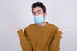 © Jihan - Puzzled and clueless young man wearing medical face mask with arms out, shrugging his shoulders, saying: who cares, so what, I don't know. Protection against infectious disease.