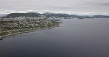 Forward Approaching Aerial Footage Of A Luxurious Cruise Ship Leaving The Port Of Alesund, The Most Beautiful Town Of Norway, While A Tugboat Performs A Water Salute By Spraying Water In The Air.