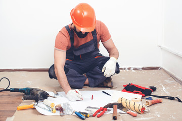 Handyman writing a plan of work. Builder wears safety helmet. Builder tools on a floor. House renovation service.