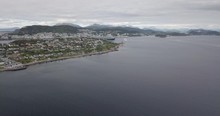 Forward Approaching Drone Footage Of A Luxurious Cruise Ship Leaving The Port Of Alesund, The Most Beautiful Town Of Norway, While A Tugboat Performs A Water Salute By Spraying Water In The Air.