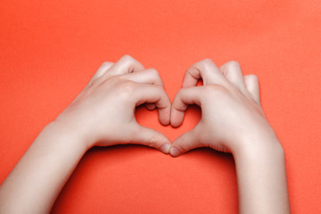 Child make a heart on a red background.