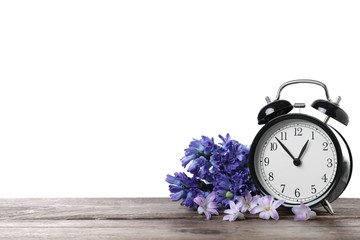 Poster - Black alarm clock and spring flowers on wooden table against white background, space for text. Time change