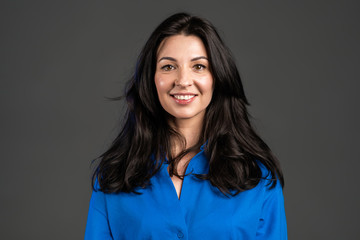 Charming mature woman isolated on grey studio background. Portrait of adult lady with long hair in blue shirt with smile looking to camera.