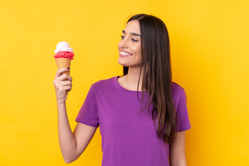 Wall Mural - Young brunette woman with a cornet ice cream over isolated yellow background with happy expression